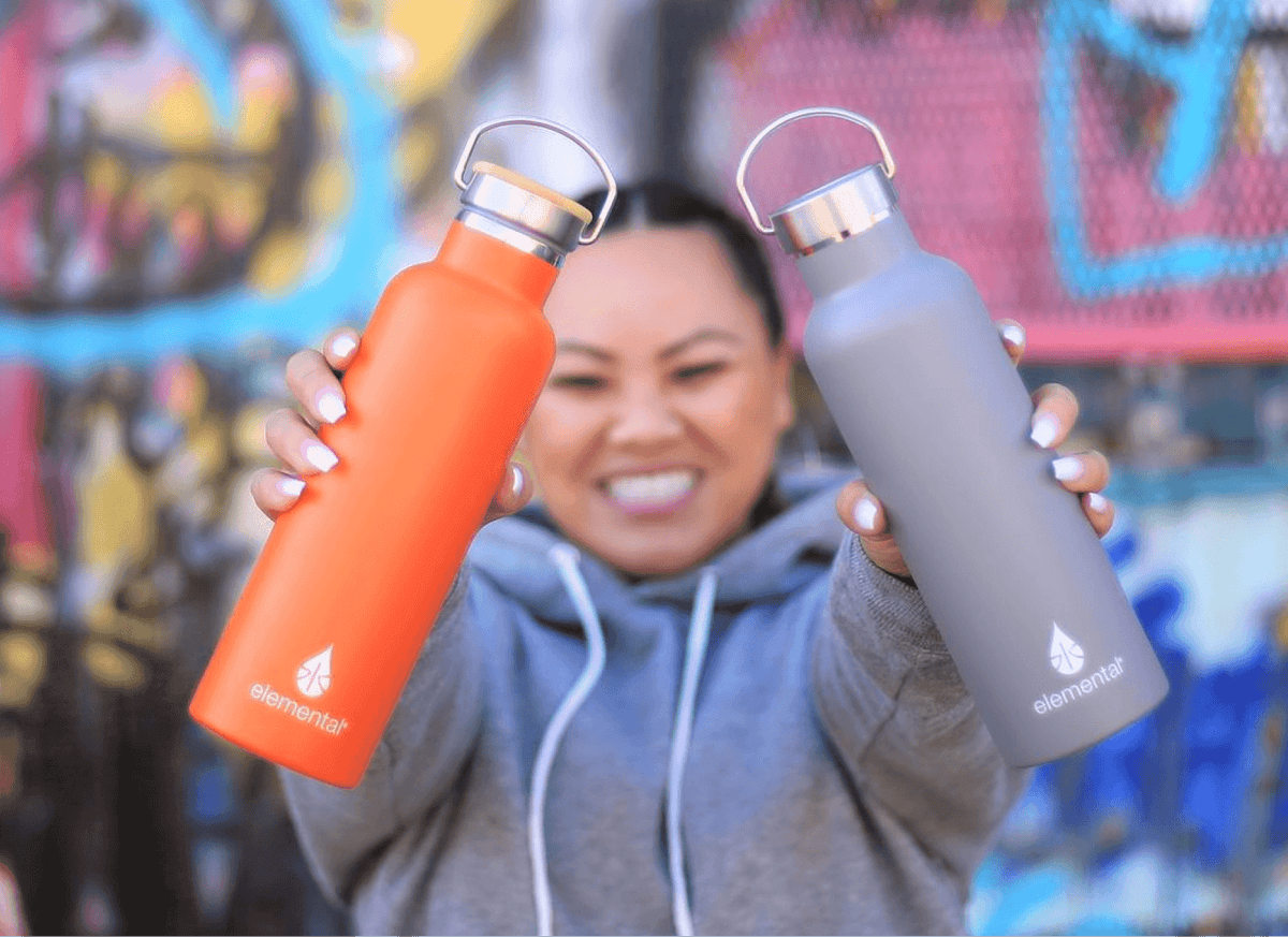 Smiling woman holding up orange and gray Elemental bottles